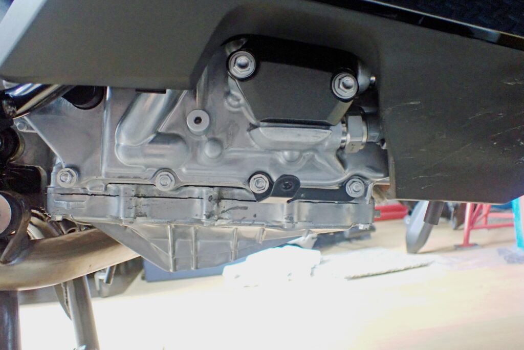 The right-side engine case of a Honda X-ADV completely exposed after cowl removal, revealing the black triangular DCT oil filter cover.