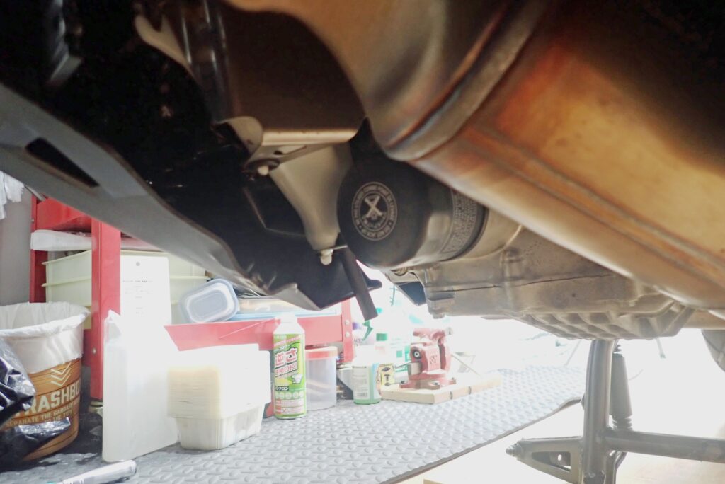 Under-engine view of a Honda X-ADV with the skid plate removed, completely exposing the black spin-on engine oil filter cartridge.