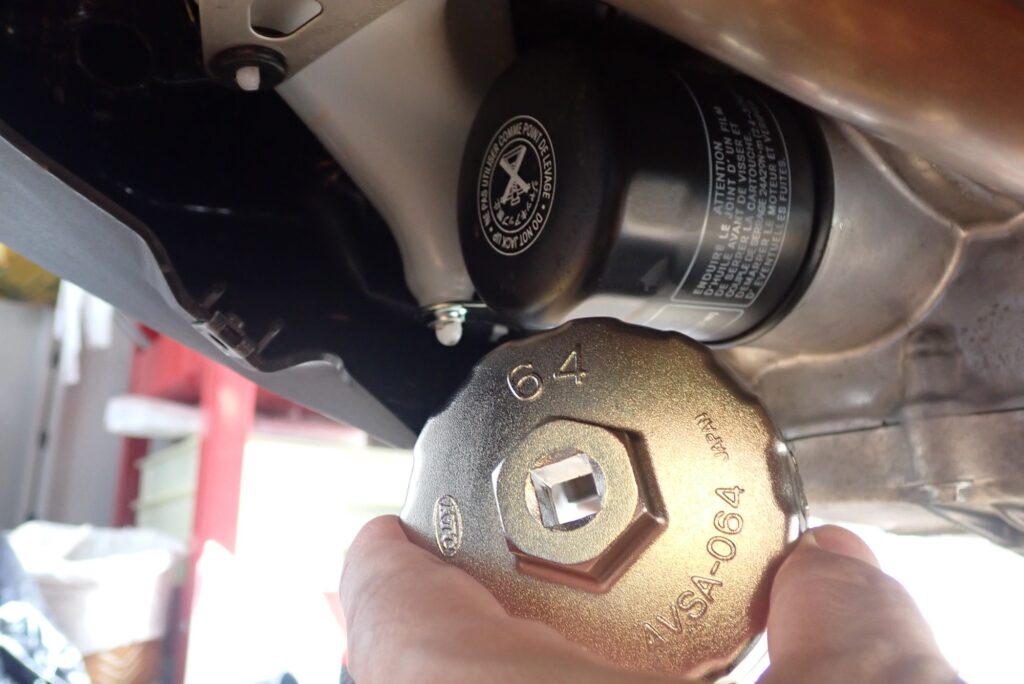 Fitting a silver KTC AVSA-064 oil filter cup wrench onto the black spin-on oil filter cartridge under a Honda X-ADV engine.