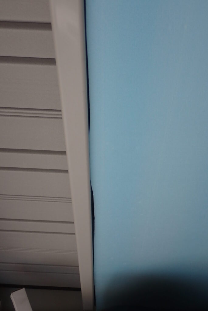 A small gap and clearance visible between the garage steel frame rail and the unevenly cut edge of the blue insulation panel.