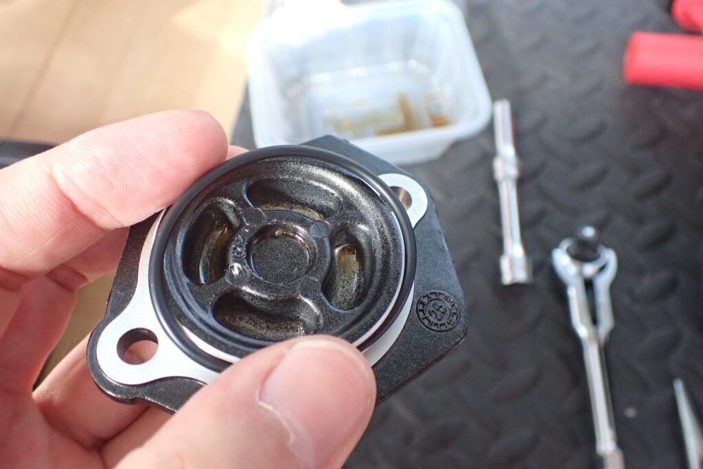 The inner backside view of a removed black Honda DCT oil filter cover, showing the round rubber sealing gasket groove.