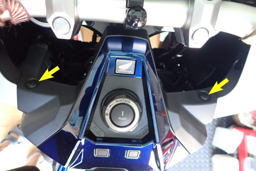 Yellow arrows pointing to the two plastic push-rivet clips located above the ignition switch panel on a Honda X-ADV.