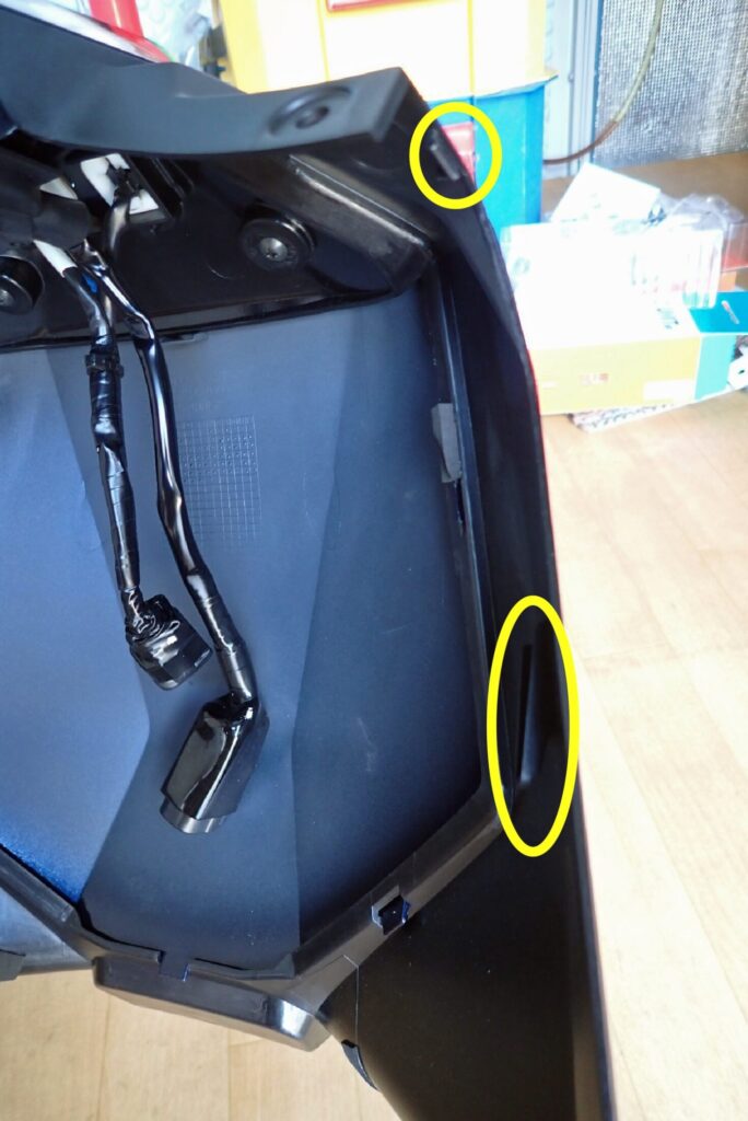 Yellow circles highlighting the side retaining slot and upper hook tab on the inner edge of the center fairing panel.