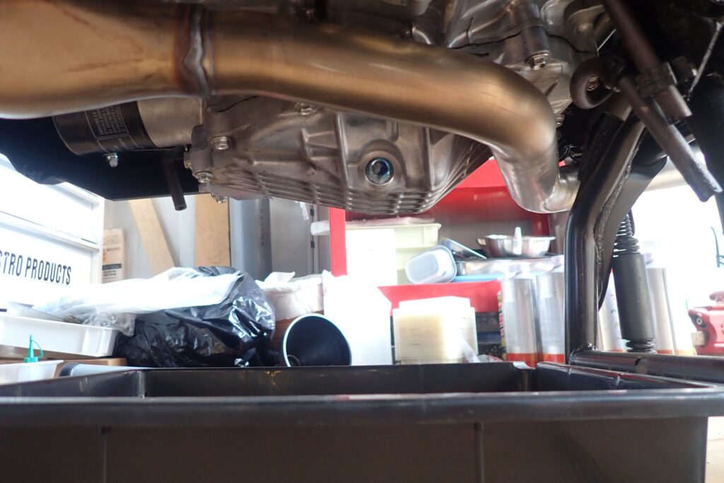Underbody view of a Honda X-ADV engine case showing the silver oil drain bolt location with the underguard removed.