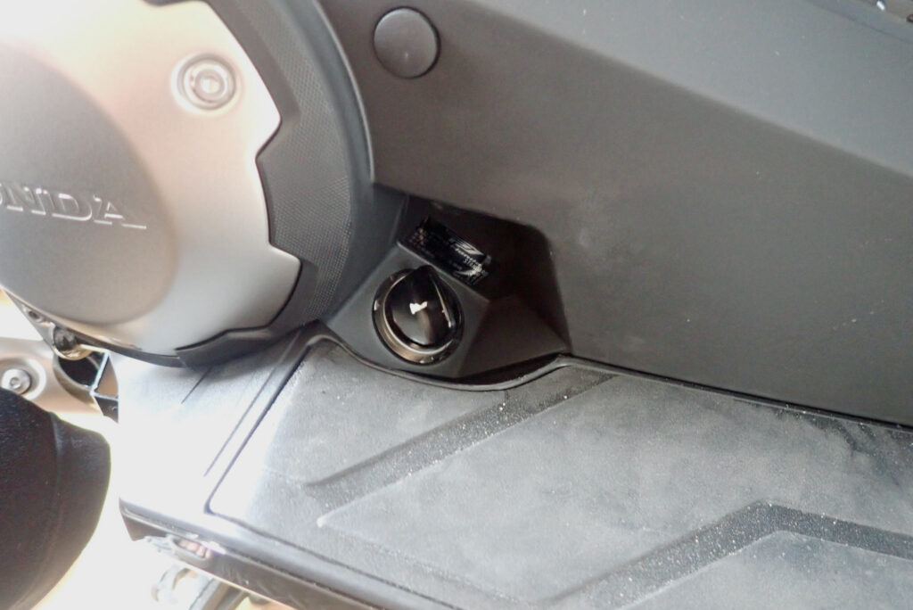 Close-up view of the black engine oil filler cap located near the right footboard on a Honda X-ADV motorcycle.