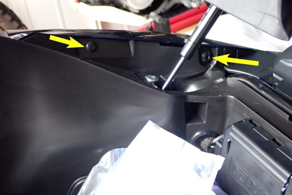 Yellow arrows pointing to the two fixing socket bolts on the inner compartment wall required to remove the rear side fairing of a Honda X-ADV.