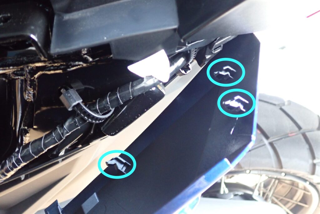 Cyan circles highlighting the three plastic sliding hooks on the inner rear edge of the fairing that require sliding the panel backward for removal.