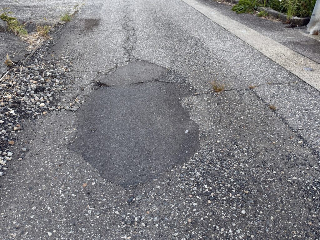 A Honda X-ADV motorcycle riding on an uneven bumpy asphalt road surface with joints and potholes.