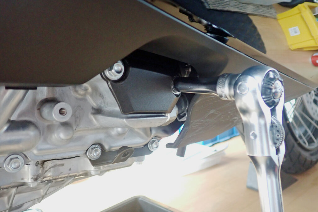 Using a socket wrench handle to loosen the hex bolts on the black triangular DCT automatic clutch oil filter cover panel.