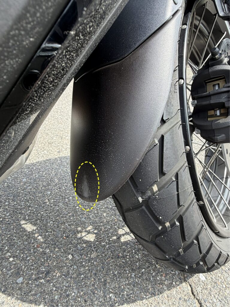 Close-up of the bottom edge of a matte black motorcycle fender extender, showing a white scratched mark from rubbing against the bike body.