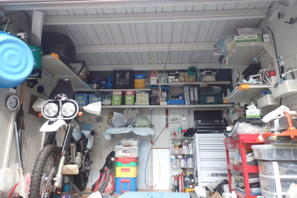 The internal view of a metal motorcycle garage before installing insulation panels, showing the exposed bare steel ceiling and storage shelves.