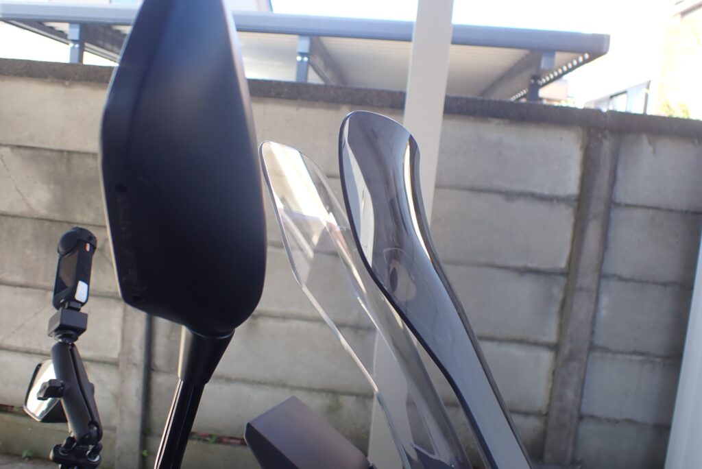 Close-up of the flipped-up spoiler top edge of an aftermarket smoked windscreen for a Honda X-ADV, designed to deflect airflow over the helmet.