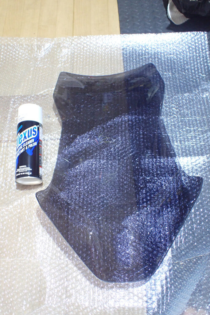 A can of Plexus plastic cleaner and protectant placed next to an aftermarket smoked windscreen for maintenance.