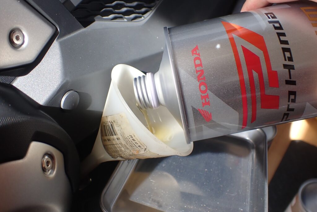Pouring fresh Honda Ultra G3 Premium Sports engine oil from a silver can into a white plastic funnel on the motorcycle.