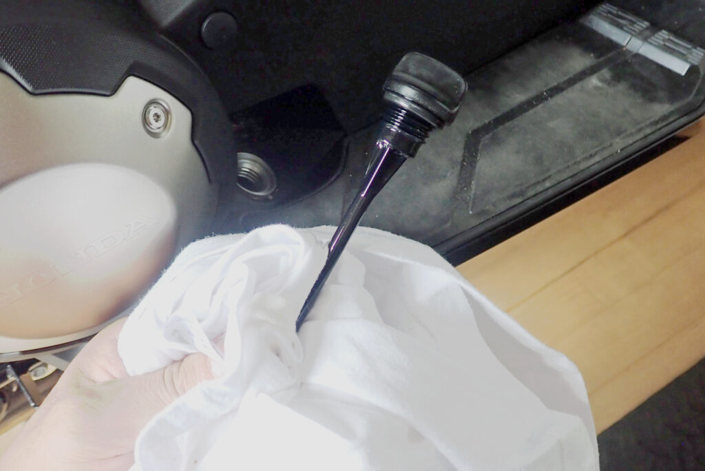 A hand pulling out the black plastic oil dipstick gauge from the Honda X-ADV engine case to check fluid level.