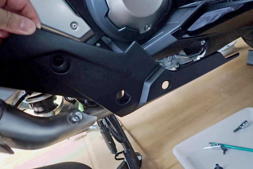 Reassembling the matte black lower side body panel cowl back onto the Honda X-ADV motorcycle chassis after oil servicing.