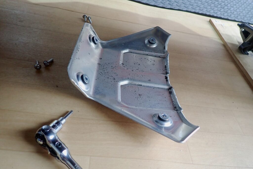 The removed aluminum underguard plate laid on the floor next to a ratchet handle, hex socket, and four mounting bolts.