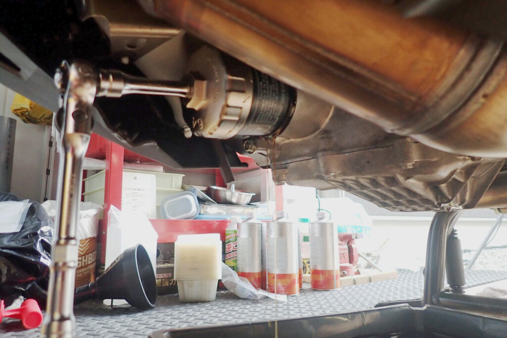 Using a socket ratchet handle and filter wrench to unscrew and remove the old dirty engine oil filter cartridge from the motorcycle.