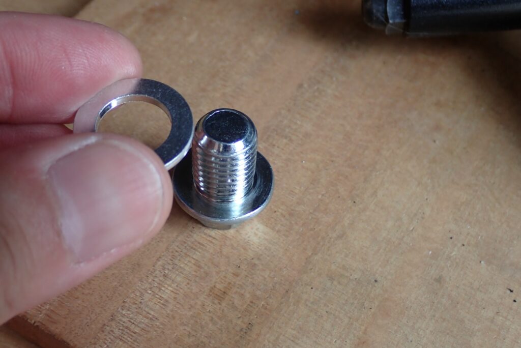 A hand replacing a used crush washer with a new silver aluminum drain gasket on a motorcycle oil drain plug.