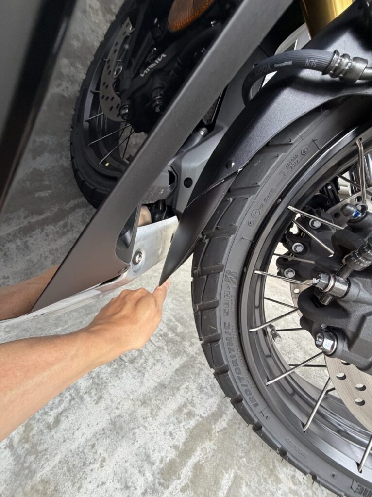 A finger pressing the edge of the attached fender extender to test clearance while stationary, showing it does not touch the body under normal hand pressure.