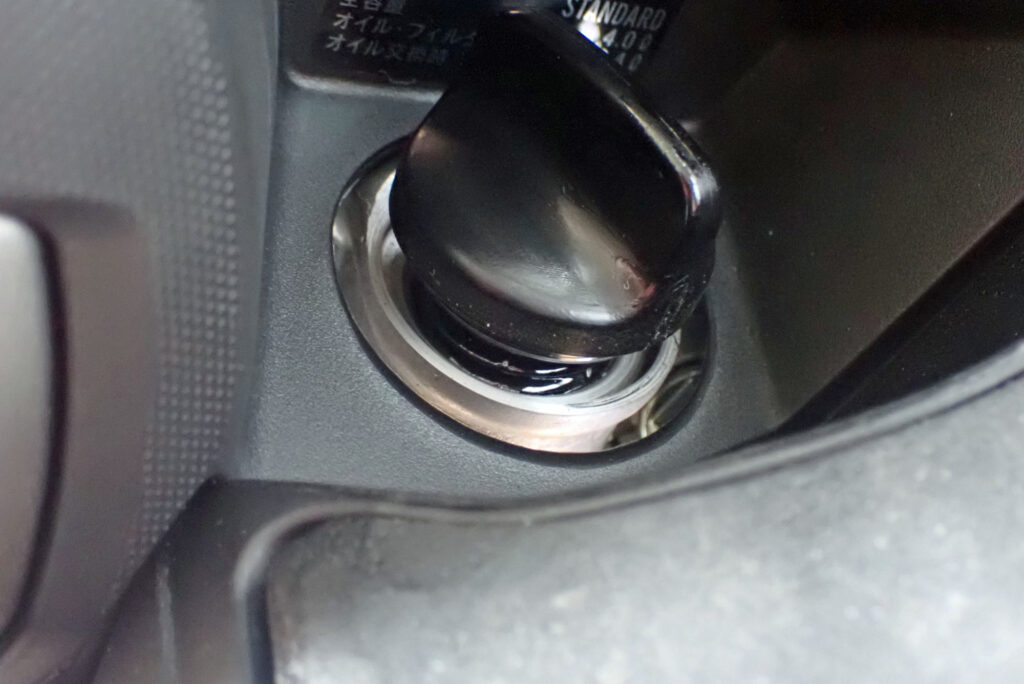 A hand tightening the black plastic oil filler cap plug back into the right side engine casing of a Honda X-ADV.