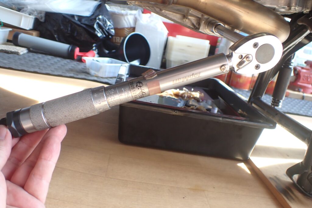 Using a silver torque wrench to secure the engine oil drain bolt plug to the factory specified torque setting.