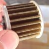 Close-up view of a used, dark brown Honda genuine DCT paper oil filter after 1000km break-in period, trapped with fine metal particles.