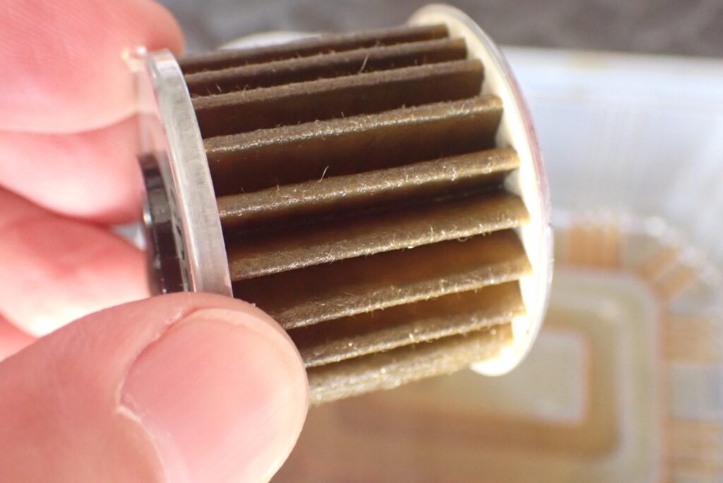 Close-up view of a used, dark brown Honda genuine DCT paper oil filter after 1000km break-in period, trapped with fine metal particles.