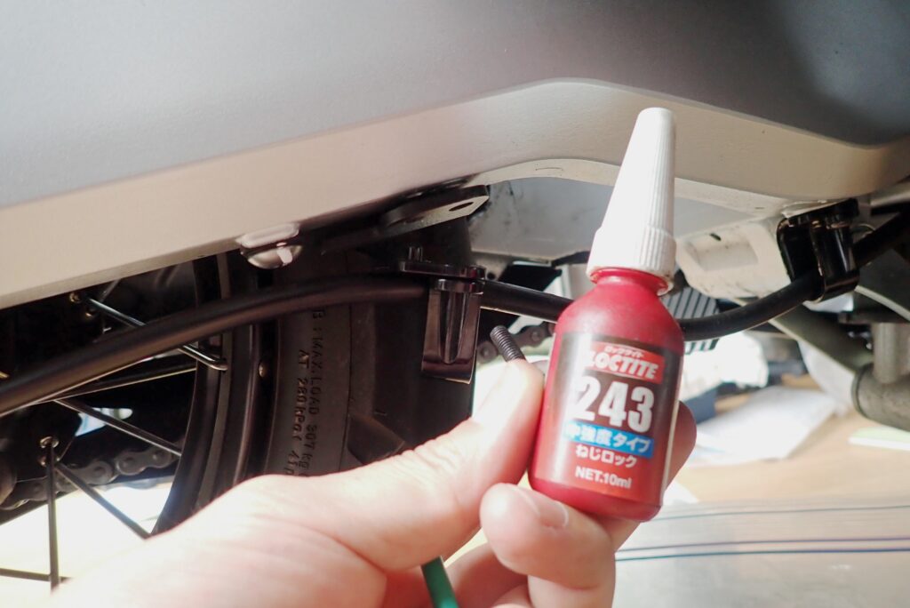 Applying Loctite 243 medium strength threadlocker to the under-swingarm bolt to prevent loosening from road vibration.
