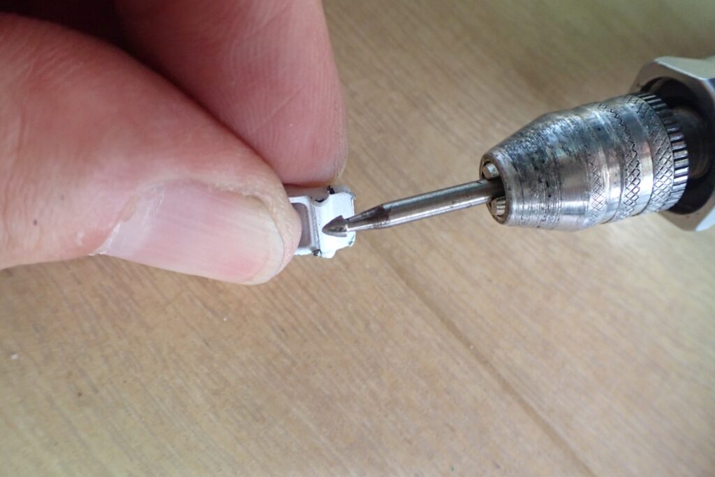 A rotary tool grinding down the steep lower hook of the broken plastic tab to facilitate easier installation and removal in the future.