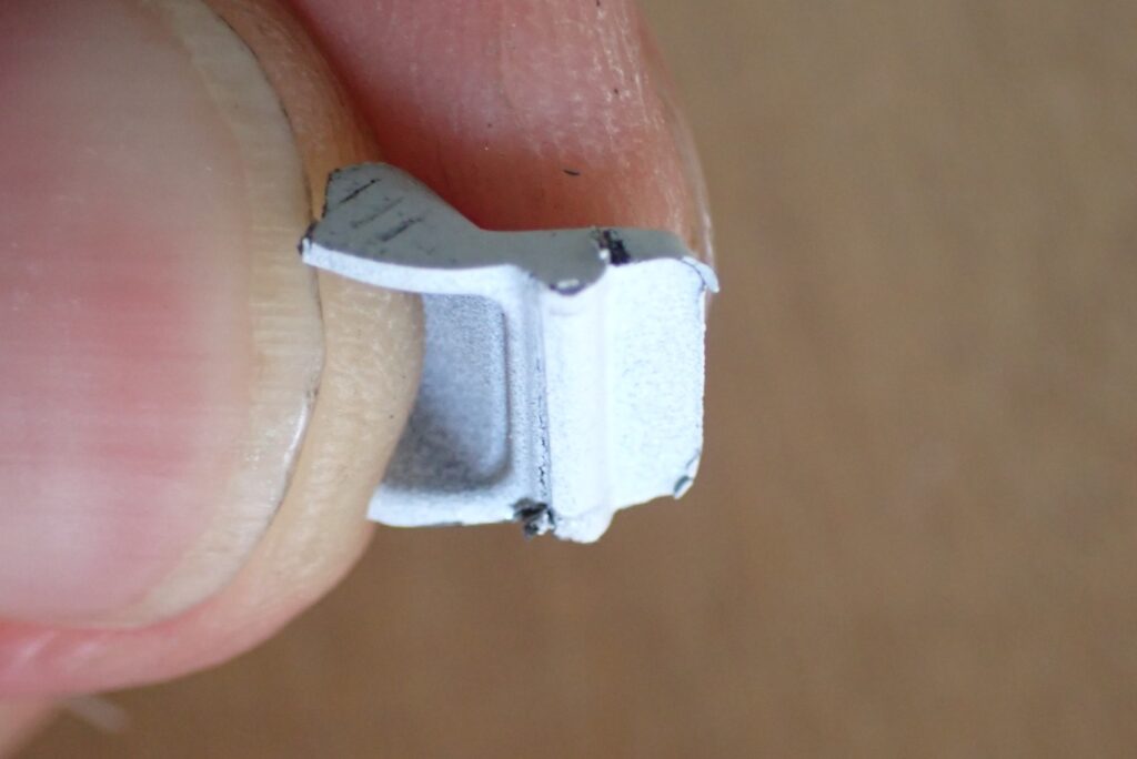 Macro photo showing the strong lower hook latch on the broken plastic cowl tab before modification, causing the removal failure.