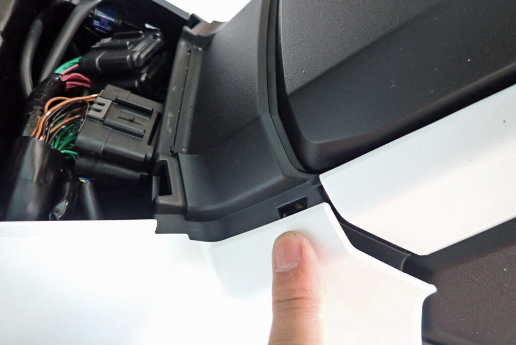 A finger pointing to the exact chassis bracket location where the side cowl locking tab broke off on a Honda X-ADV.