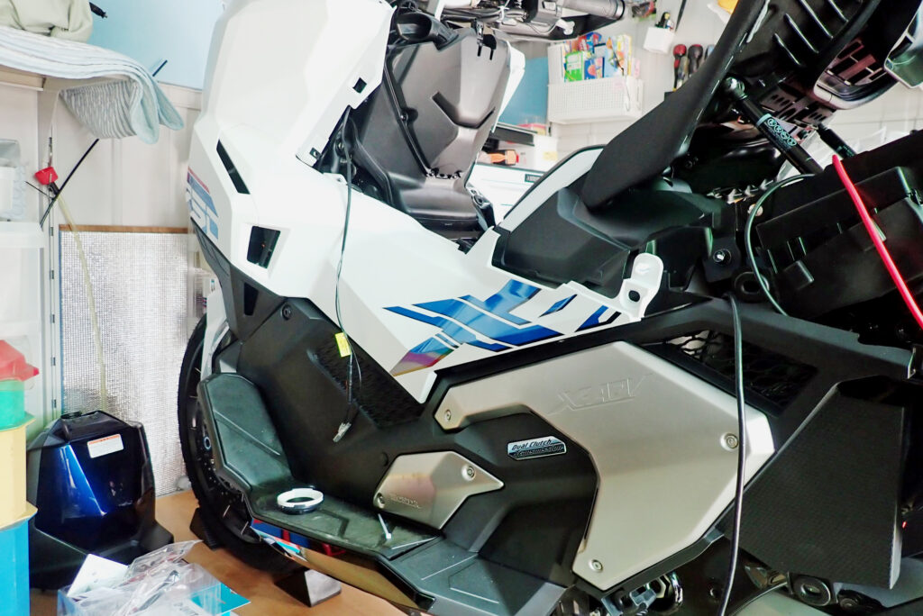 Side view of a partially disassembled Honda X-ADV motorcycle during USB power supply installation and wiring extension process.