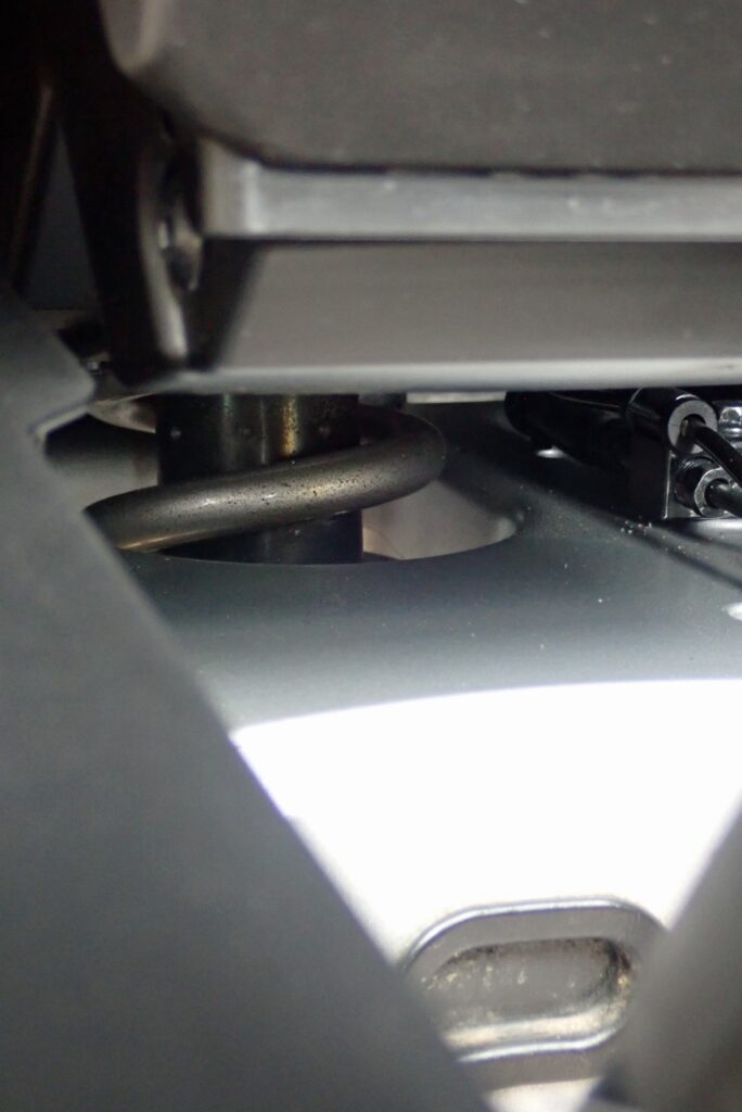 Close-up view of the exposed rear suspension shock absorber under the Honda X-ADV frame vulnerable to mud and water spray.