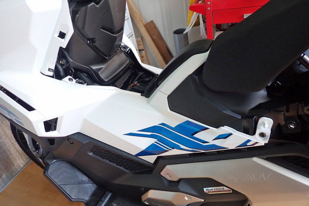 Overview of the white and blue left side body cowl panel on a Honda X-ADV motorcycle before removal.