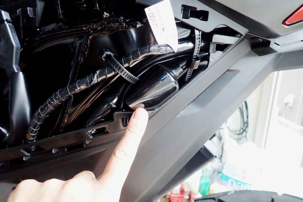 Pointing at Honda X-ADV option coupler location inside left rear cowl for Kitaco harness