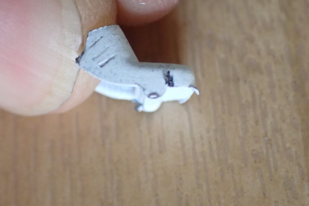 Side view of the broken Honda X-ADV fairing tab held between fingers, showing the steep retaining protrusion that resistance caused it to snap.