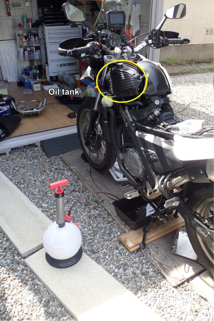 The oil tank of a dry-sump BMW G650GS, circled in yellow, with a hand-operated oil extractor.