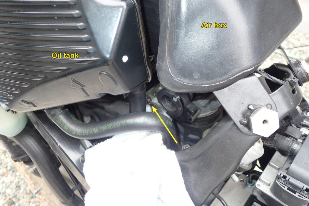 Where the throttle cable oil comes out near the throttle body of a BMW G650GS, between the oil tank and air box.
