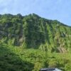 緑におおわれた高さ約500mの岩壁、悪城の壁を道路から見上げたところ
