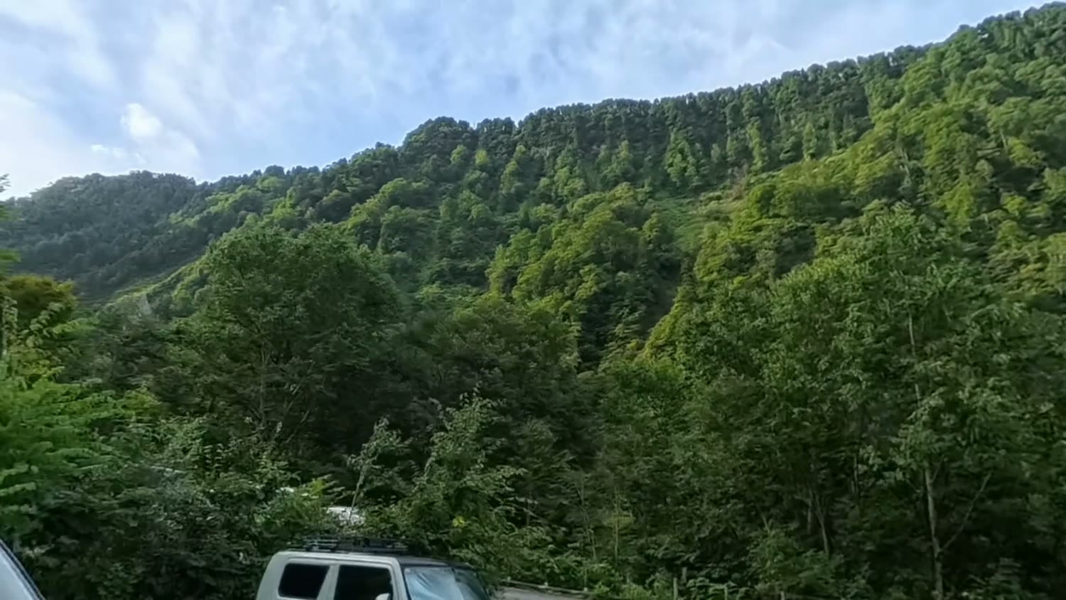 緑の山のふもとにある称名平駐車場。早朝から車がたくさん停まっている