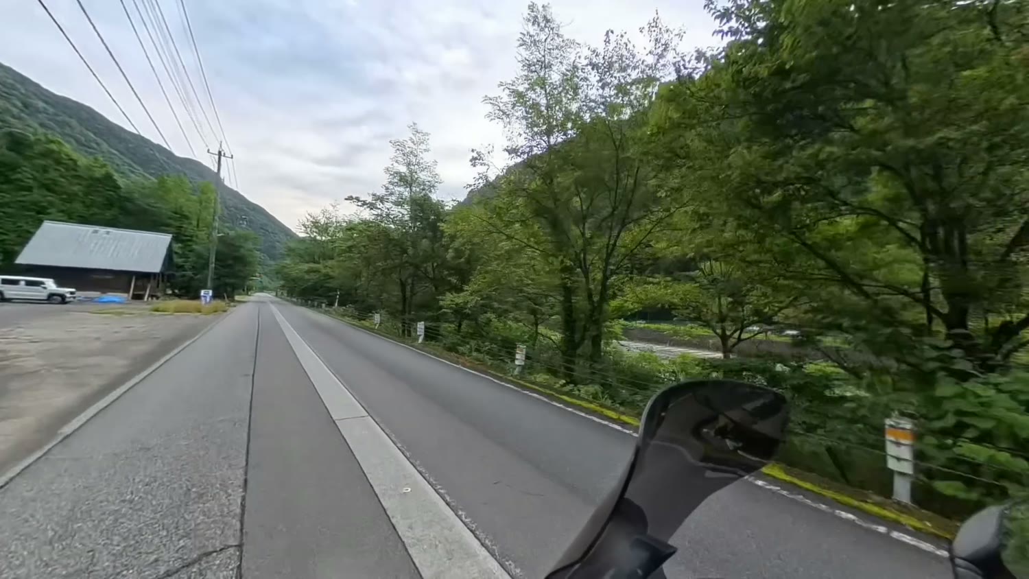緑の山にはさまれた谷あいの広い道。右手前にバイクのミラーが写っている