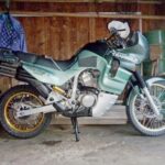 ガレージに停めたトランザルプ400V。金色のリムとオーリンズのリアサスが見える
