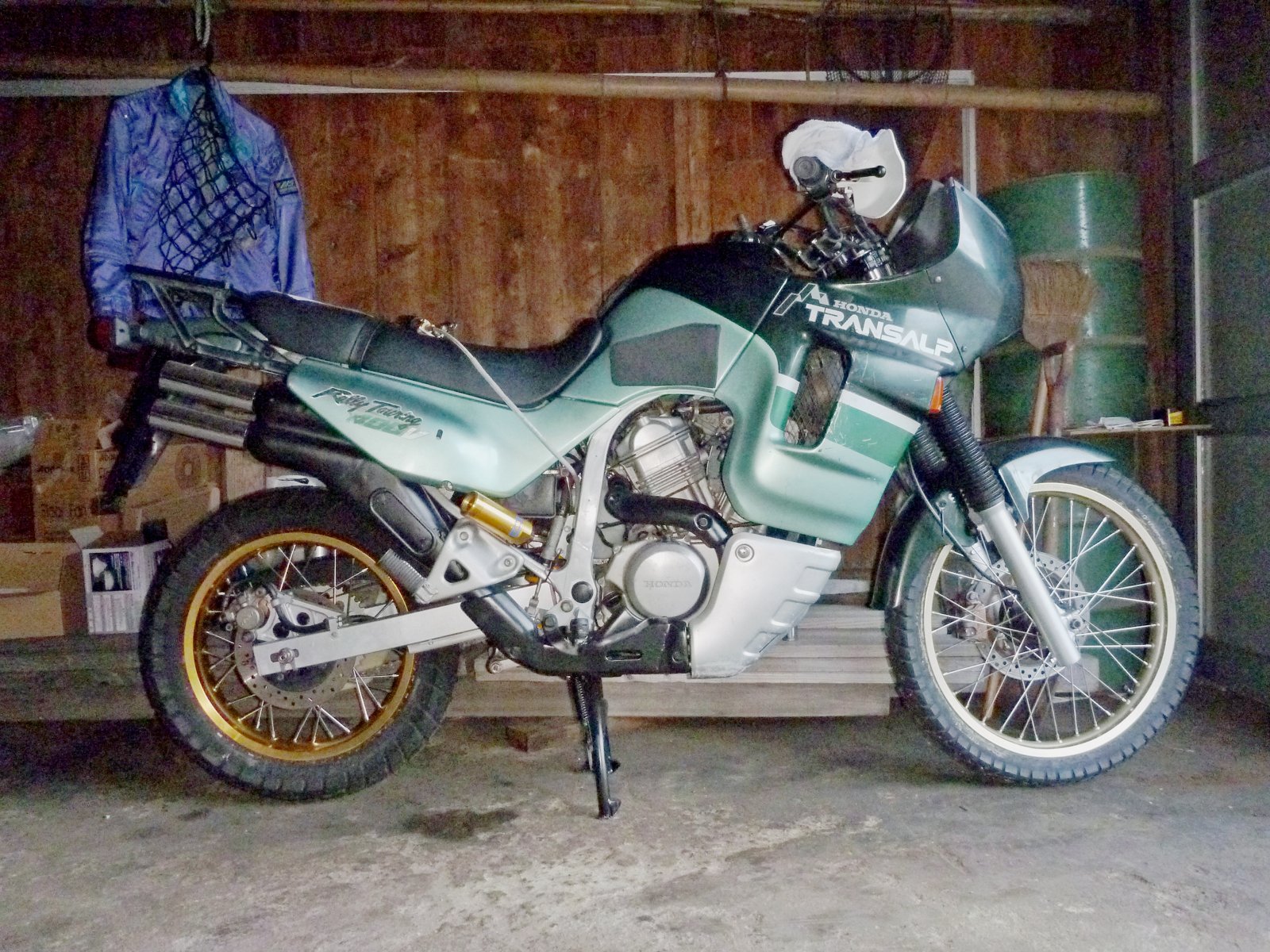 ガレージに停めたトランザルプ400V。金色のリムとオーリンズのリアサスが見える