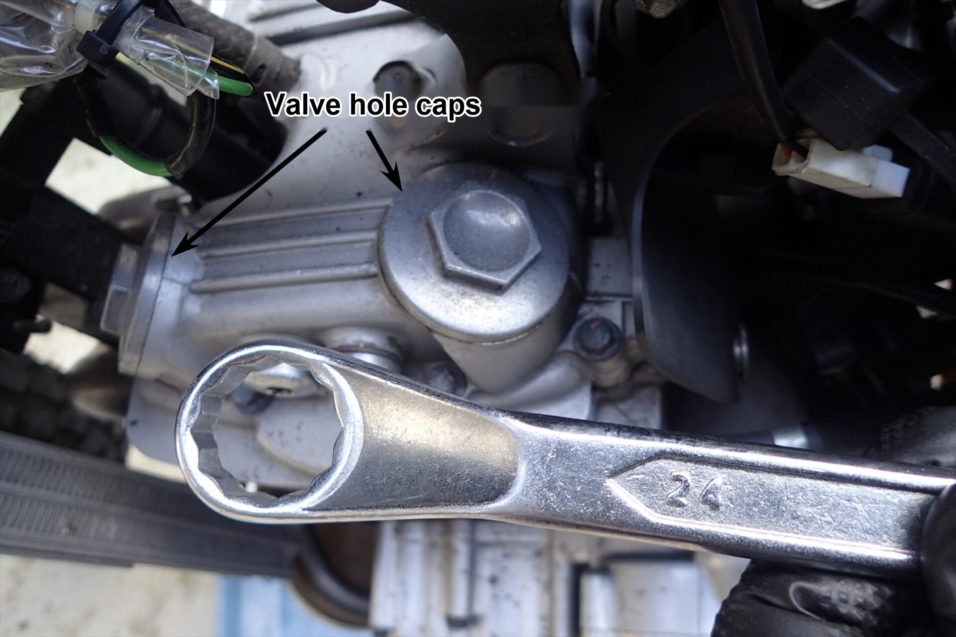 The valve hole caps on top of the XR250 cylinder head, before removing them with a 24 mm spanner.